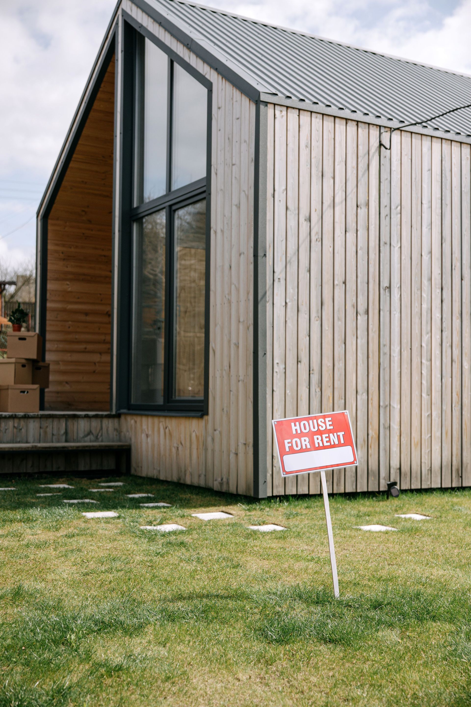 Modern wooden house with large windows and a small red sign on the lawn.