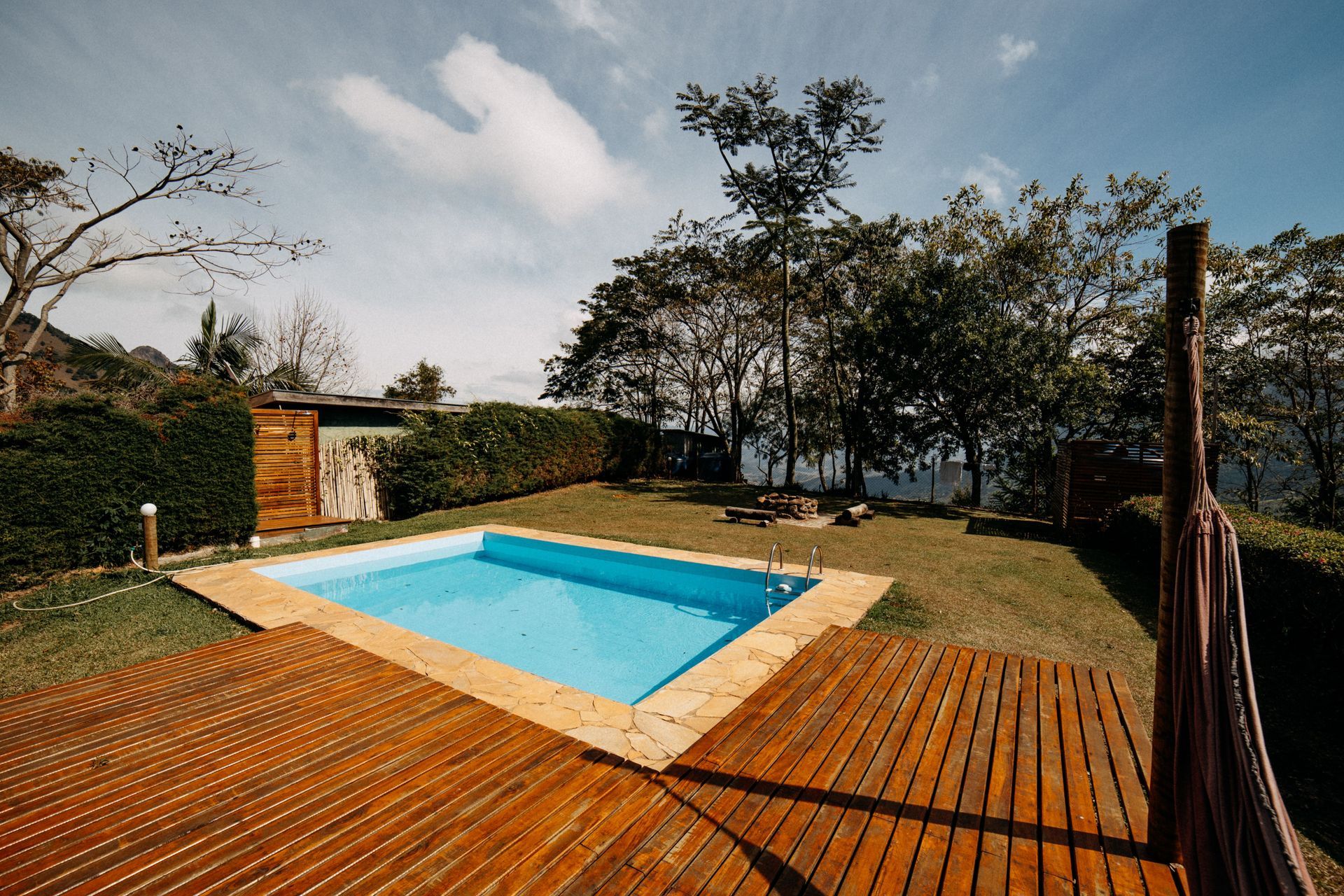 Backyard pool with wooden deck, trees, and blue sky