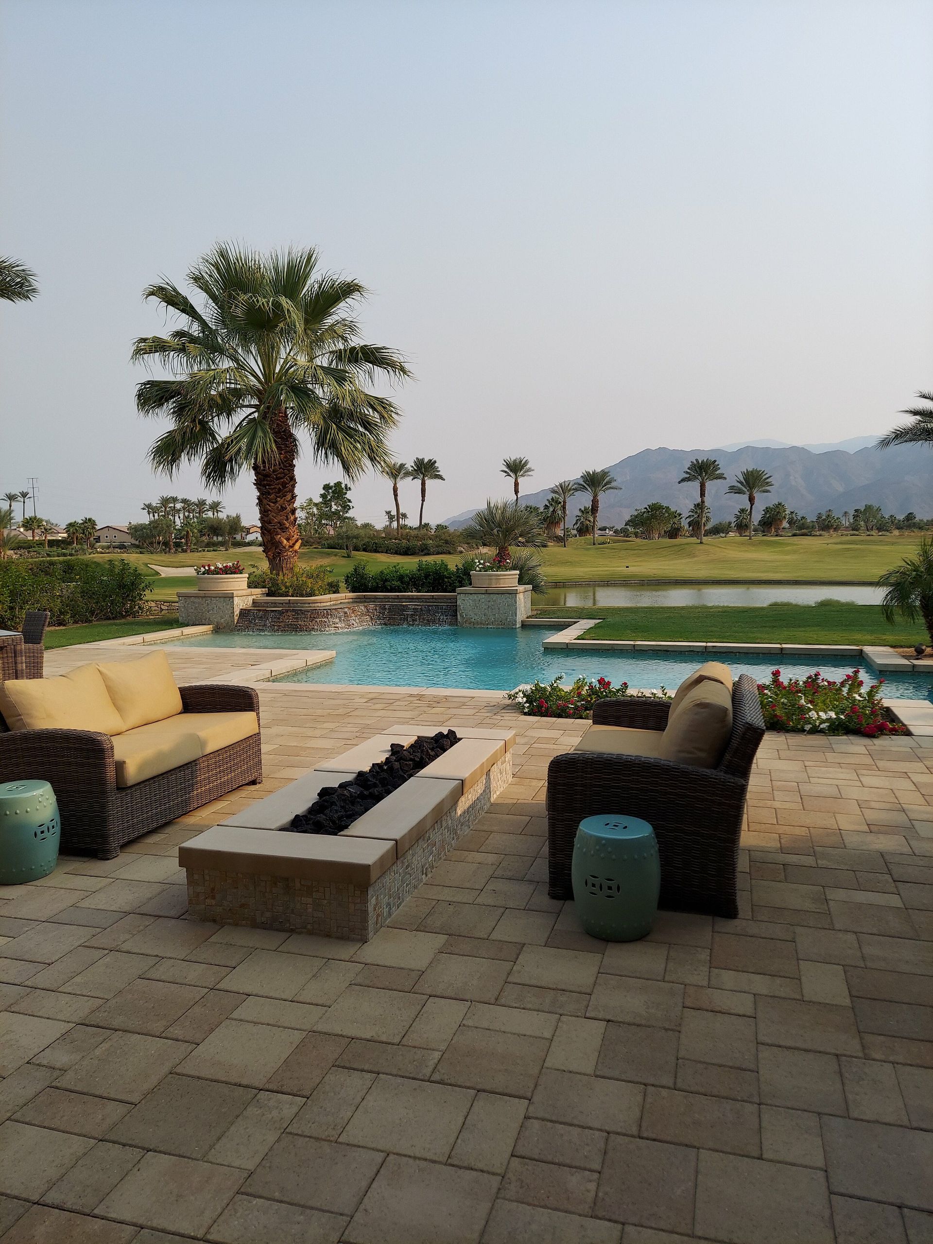Resort patio with wicker chairs, fire pit, palm trees, and a pool at sunset
