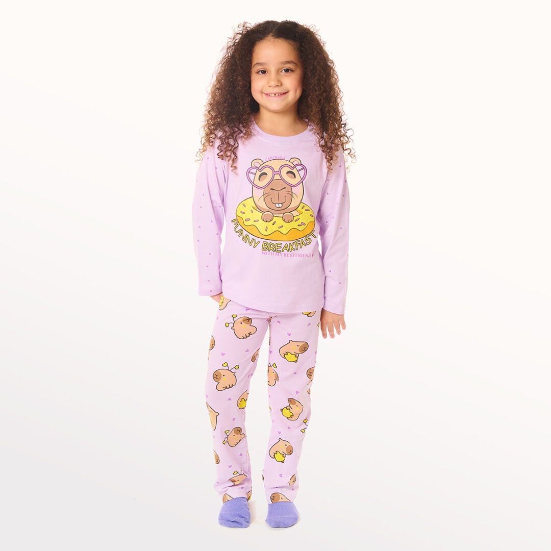 Niña con pijama de estampado de búho morado de pie sobre un fondo blanco.