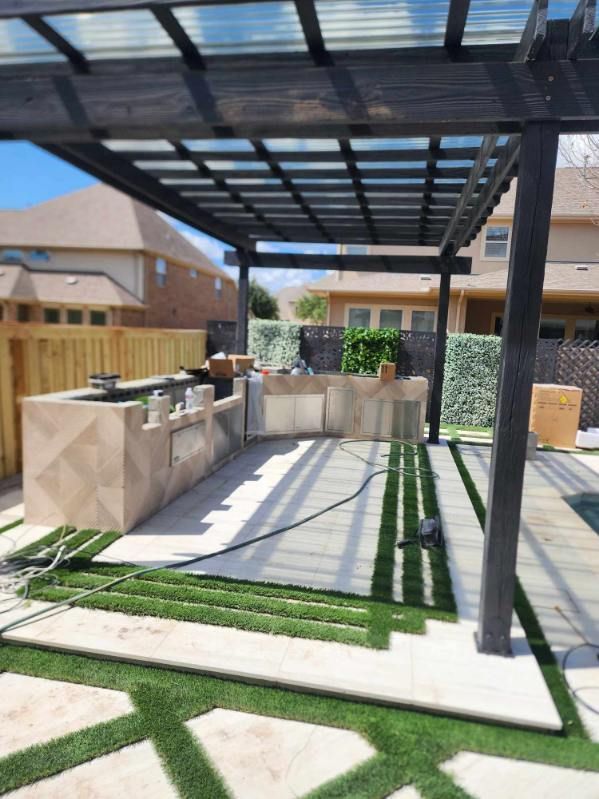 Outdoor kitchen with pergola, light-colored countertops, and artificial grass accents.