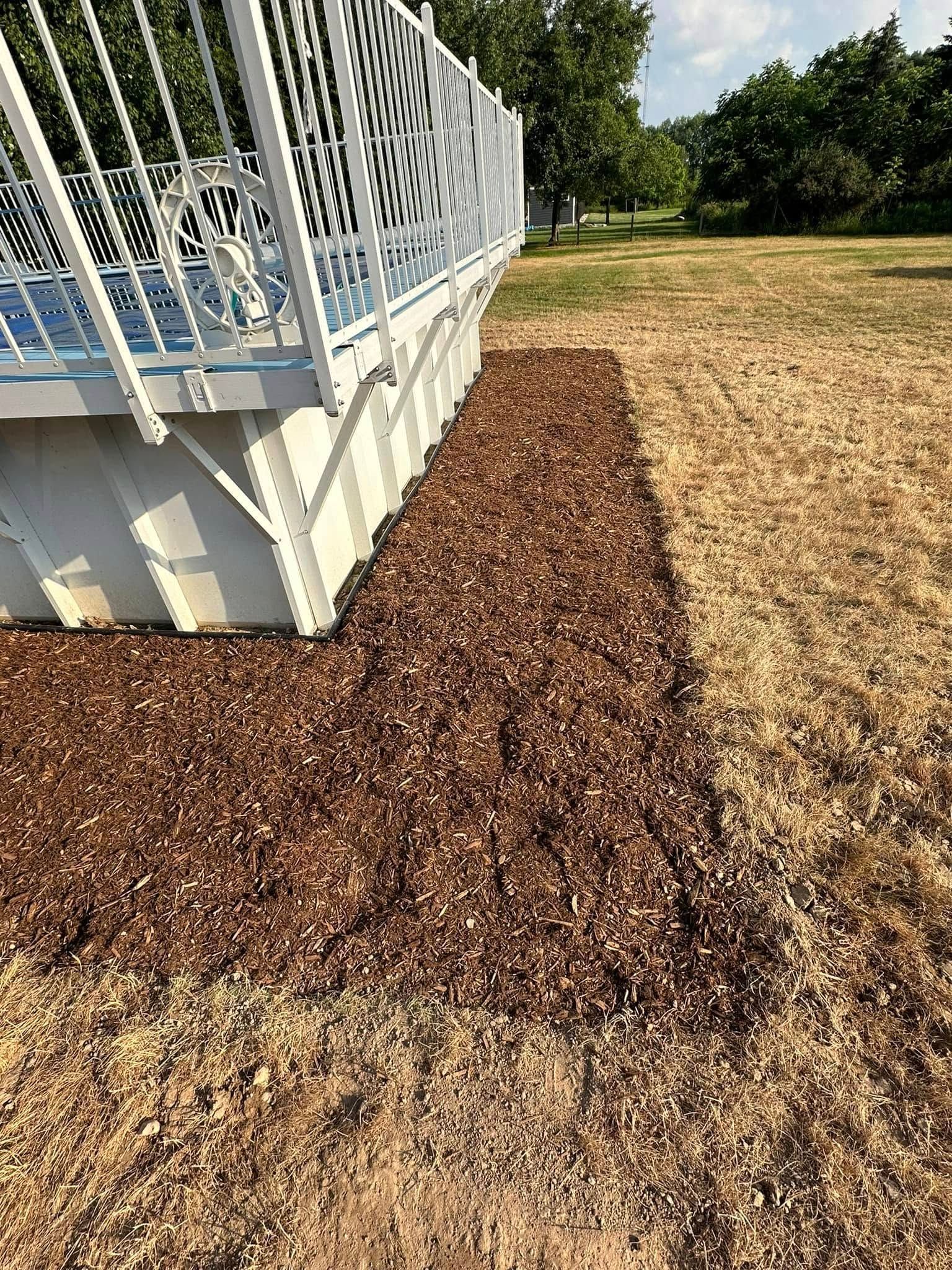 Brown mulch bed alongside a white-railed deck on a grassy lawn.