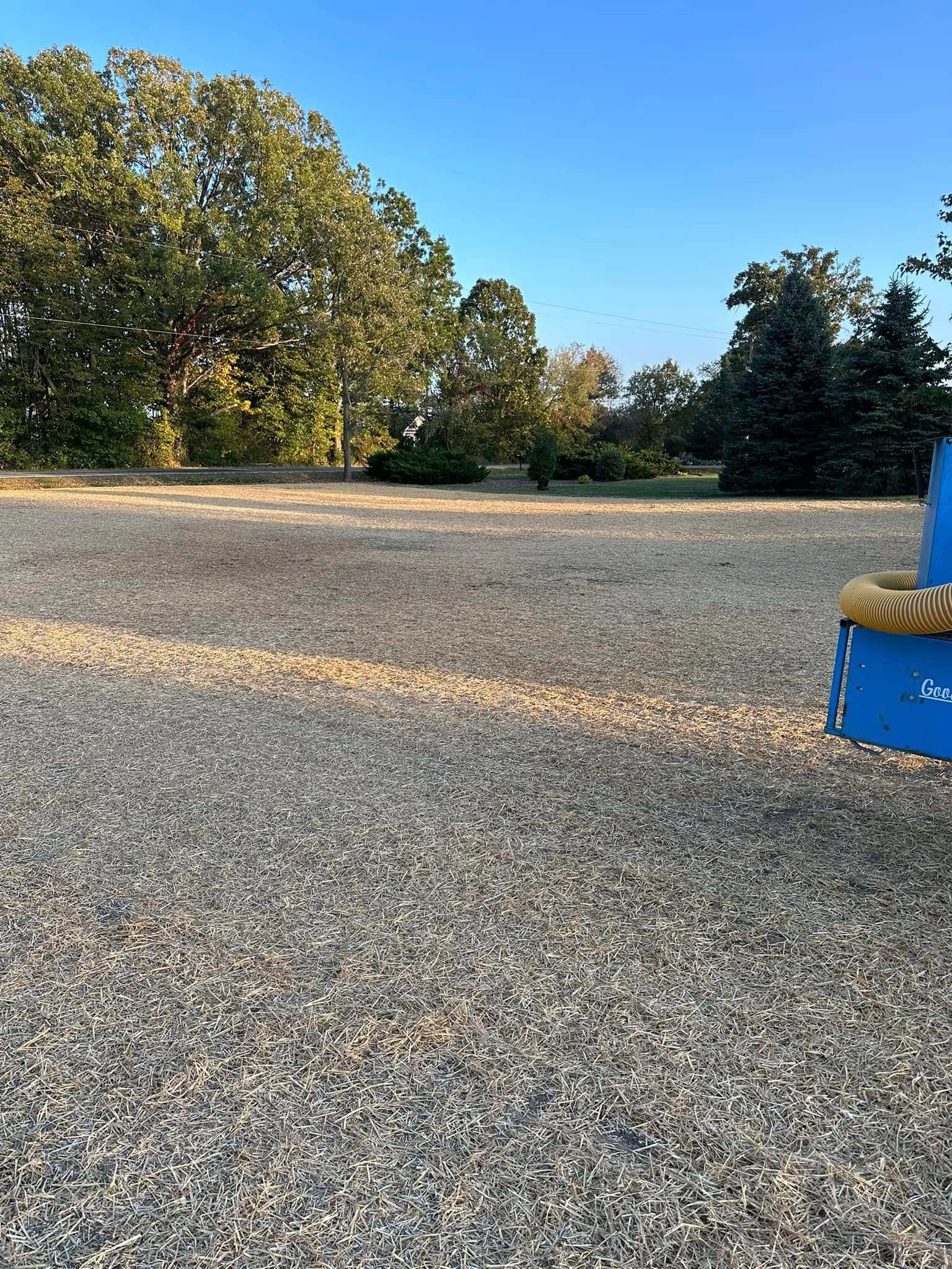 Gravel playground with trees in background under a blue sky, sun casts shadows across the ground.