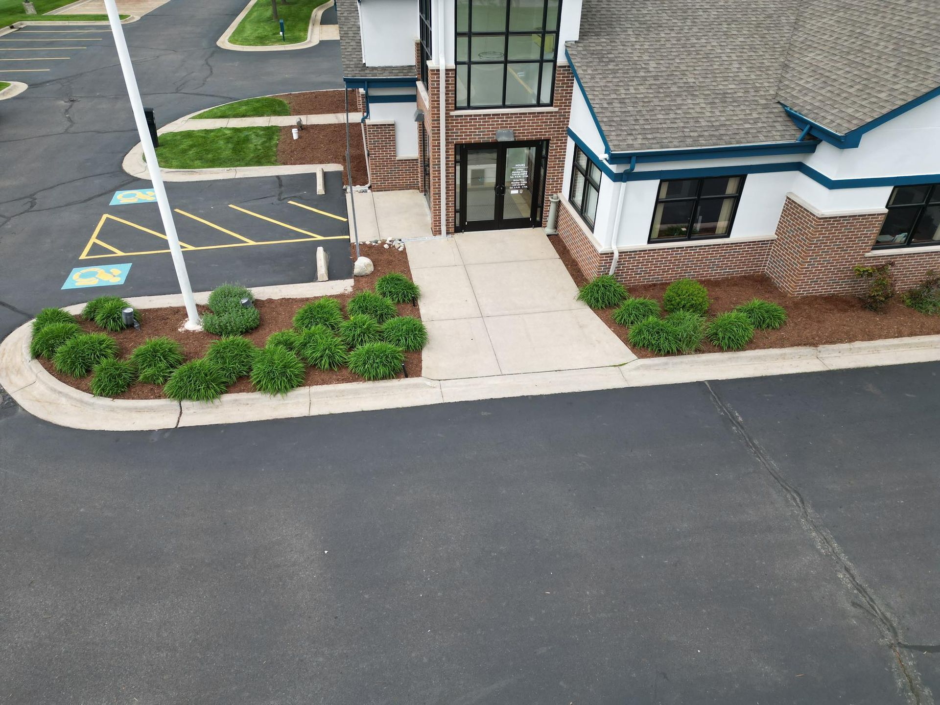 Exterior view of a building with a paved path, landscaping, and accessible parking spaces marked with blue symbols.