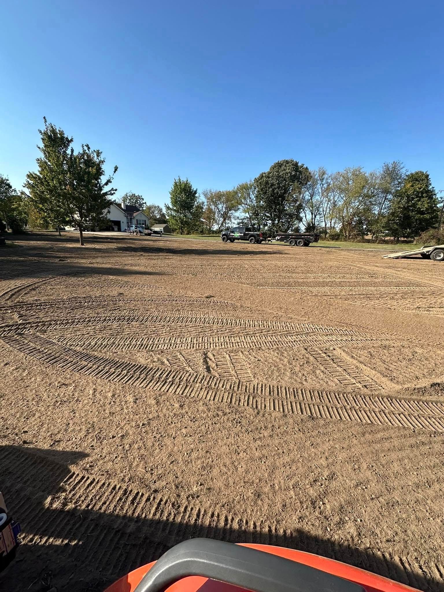 Cleared, graded lot under a clear blue sky, with trees in the background.