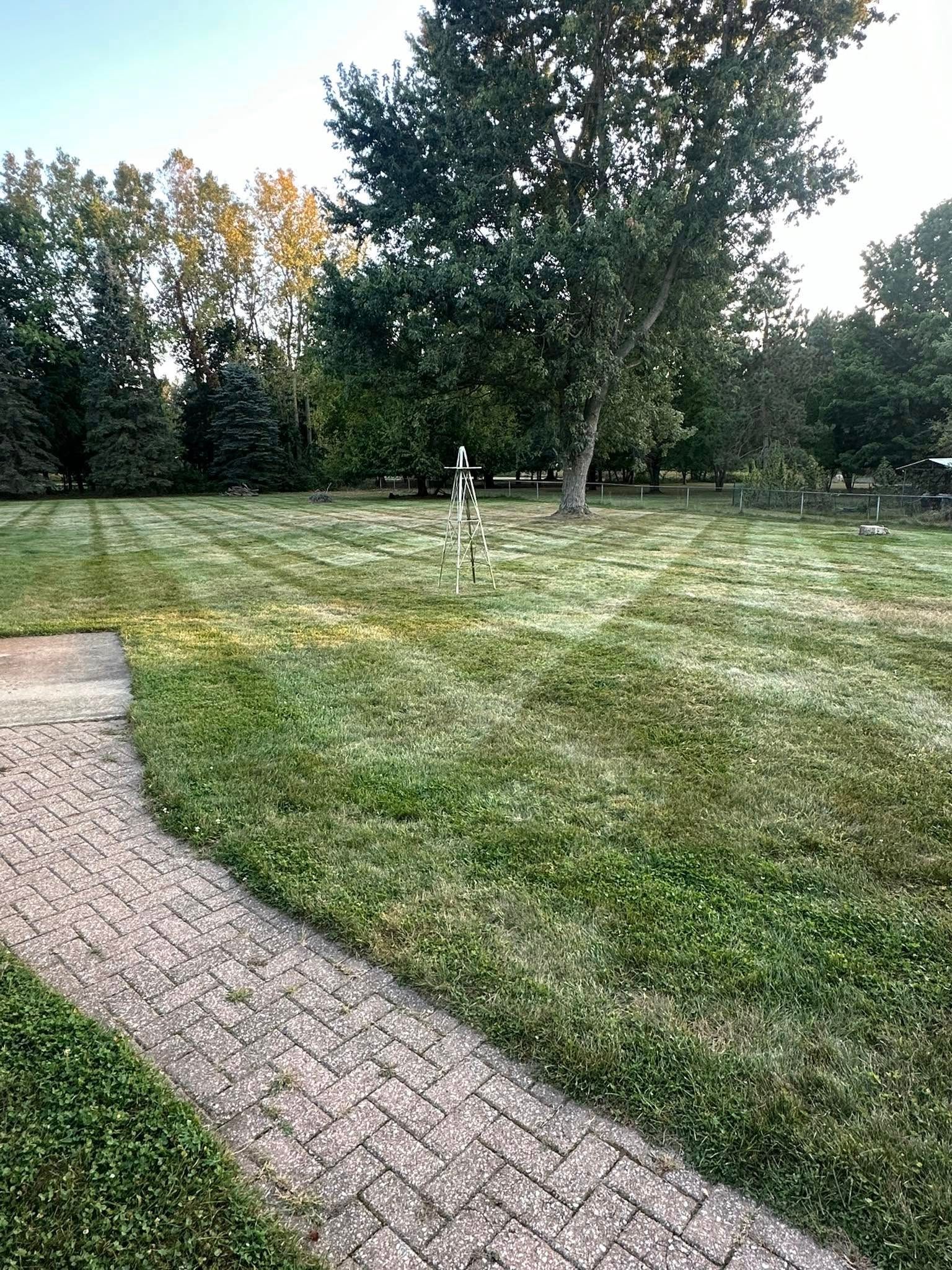 Brick pathway leads to a grassy lawn with trees in the background under a blue sky.