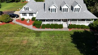 Green grass next to a tan building with a white door and window; a second, darker building is in the background.