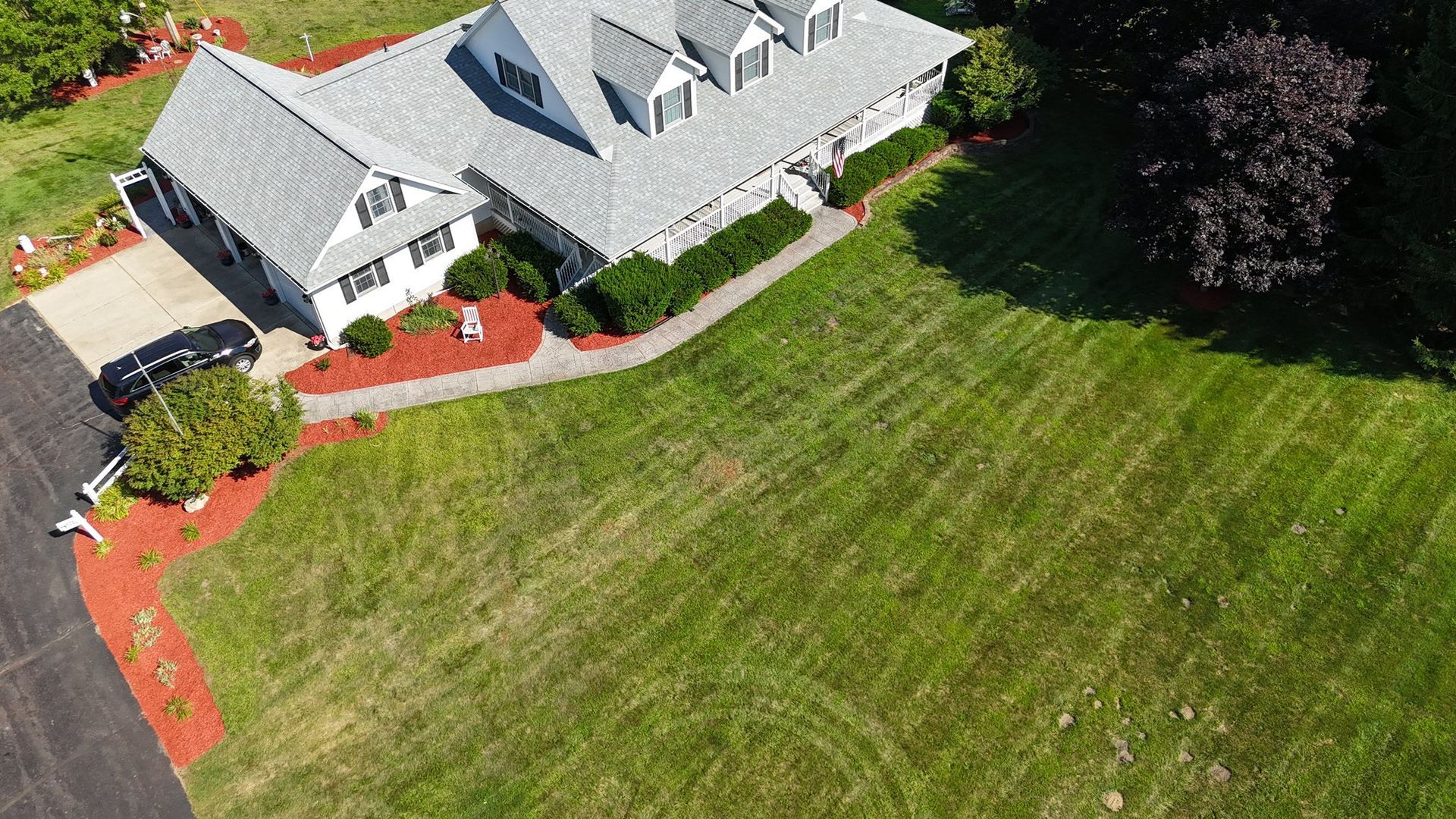 Aerial view of a gray-roofed house with a large green lawn and red mulch landscaping.