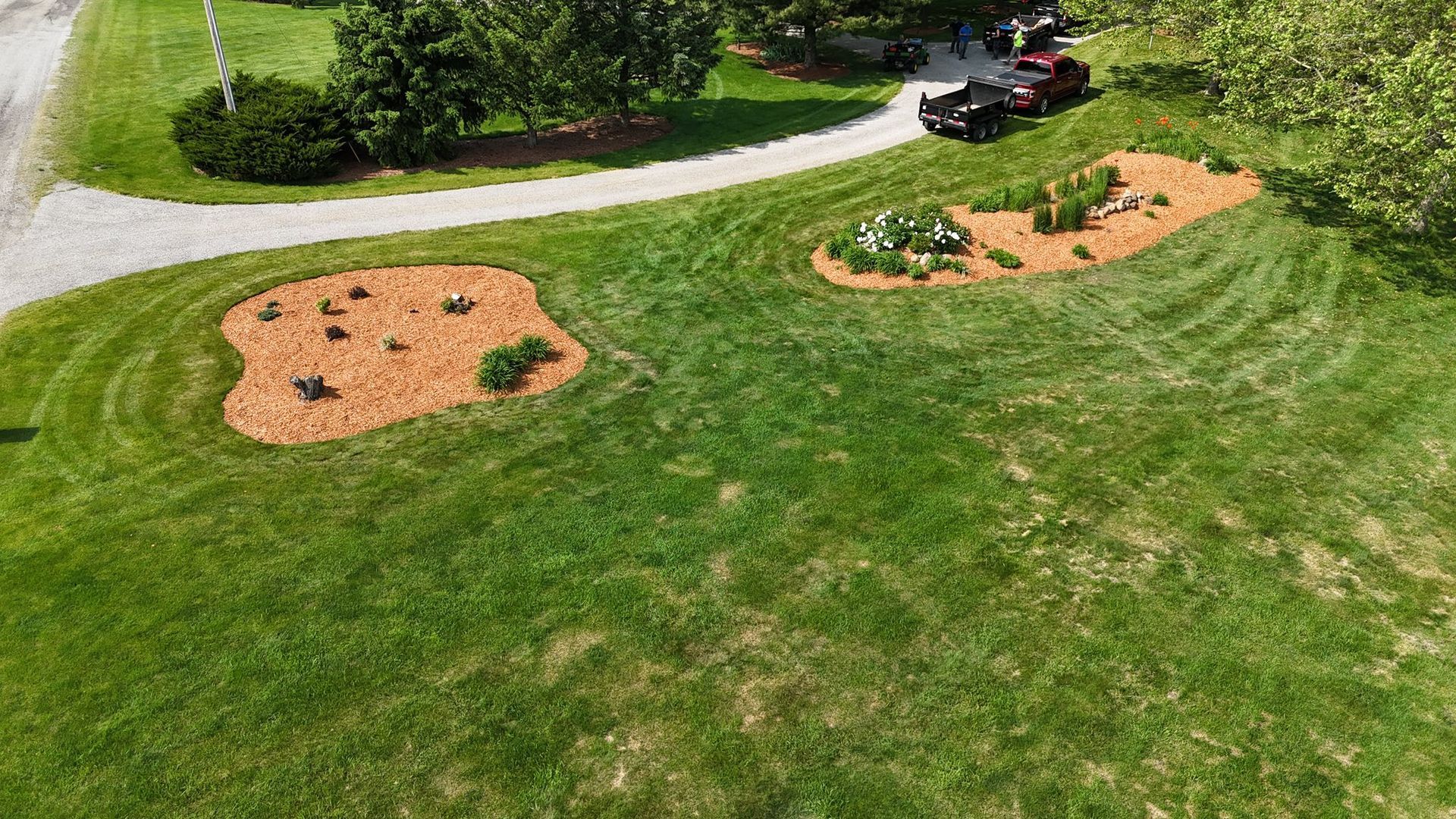 Lawn with two mulch-covered flower beds, gravel driveway, and a vehicle.