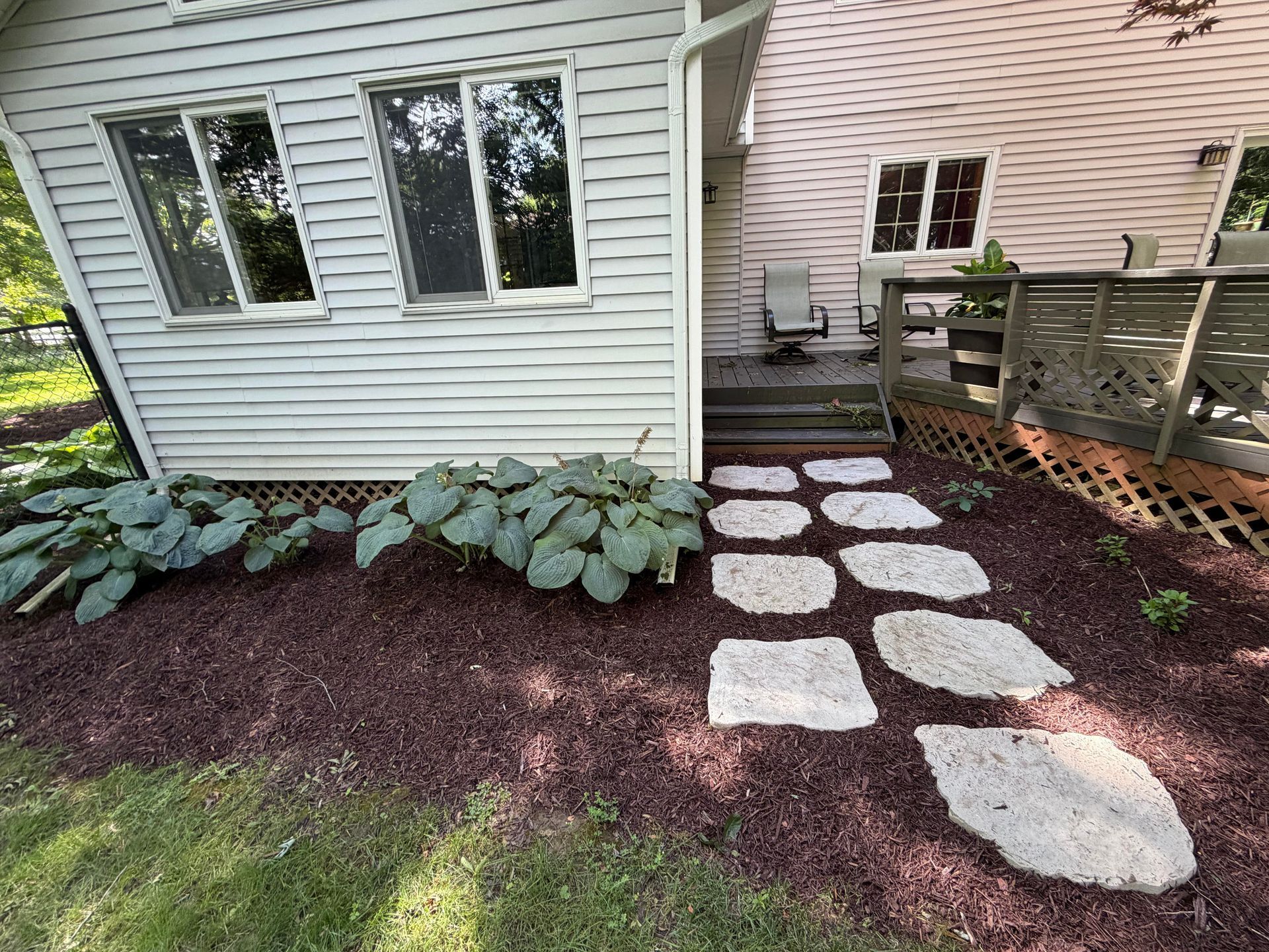 Stepping stone path beside a house, bordered by hostas and leading to a wooden deck