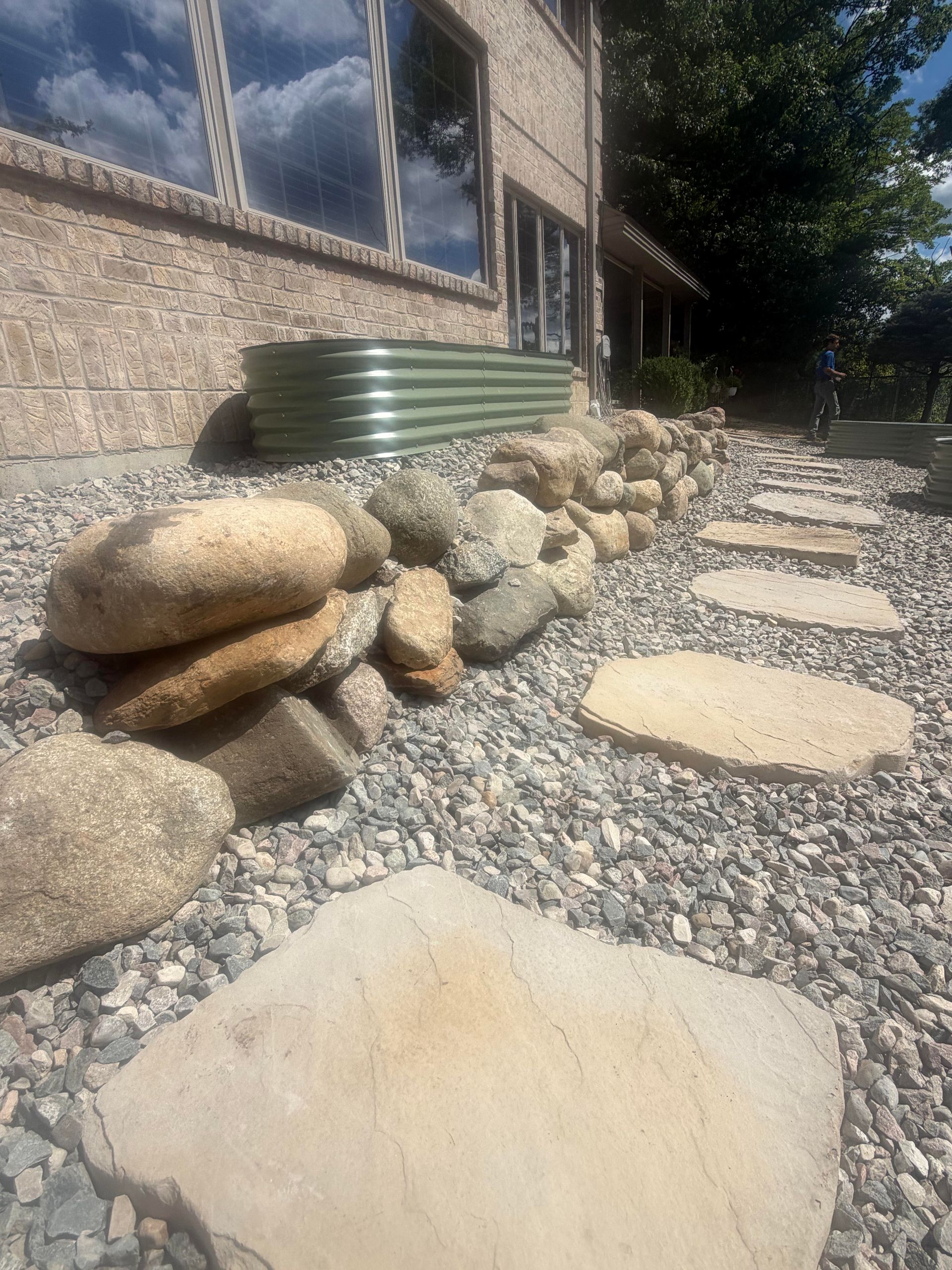 Stone path beside house with gravel border, large rocks, and a green rainwater tank.