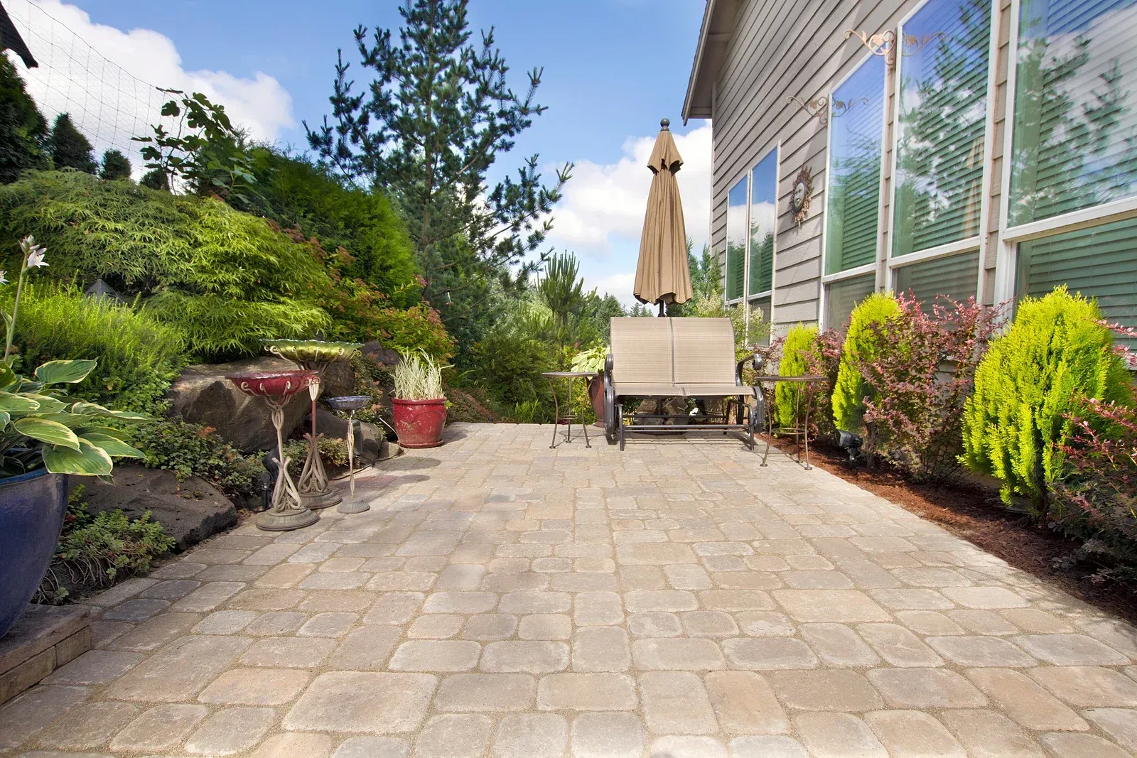 Paver patio with outdoor furniture, landscaping, and house in background. Sunny day.
