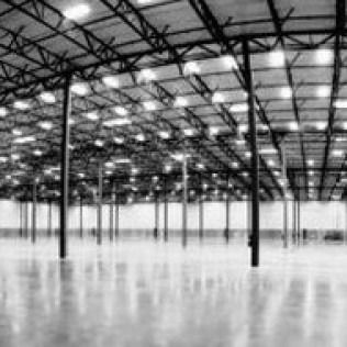 Empty warehouse interior with steel columns, bright overhead lights, and a polished concrete floor