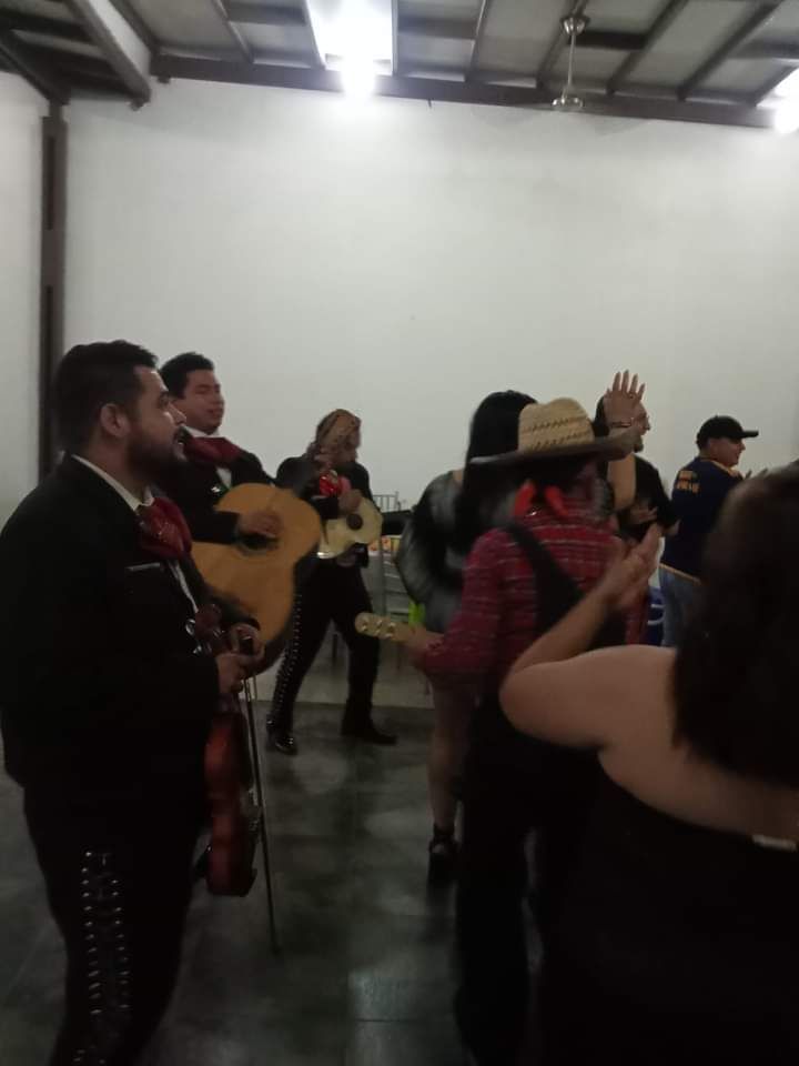 Una banda de mariachis se presenta en un evento, se la ve cerca de gente bailando.