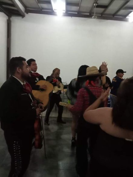 Una banda de mariachis se presenta en un evento, se la ve cerca de gente bailando.