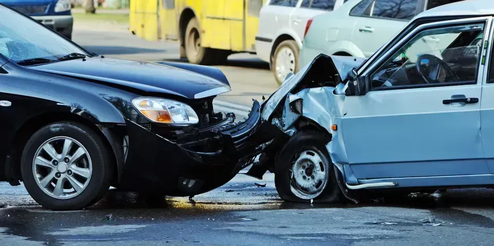 A black car and a light-colored car involved in a head-on collision on a city street.