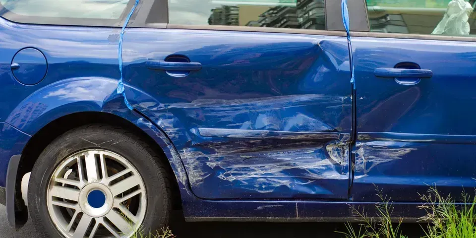 A blue car showing significant side-impact damage to the rear passenger door and panel.