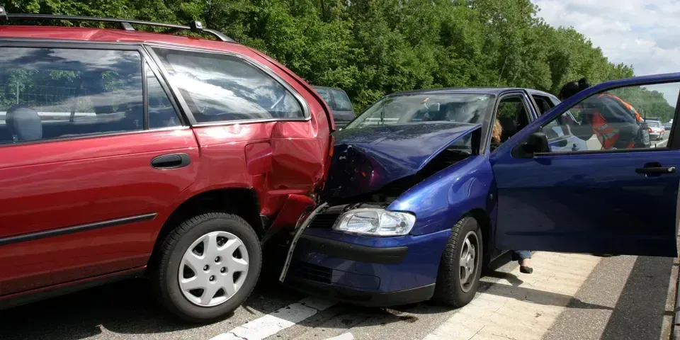 A blue sedan has crashed into the rear of a red station wagon on a road.