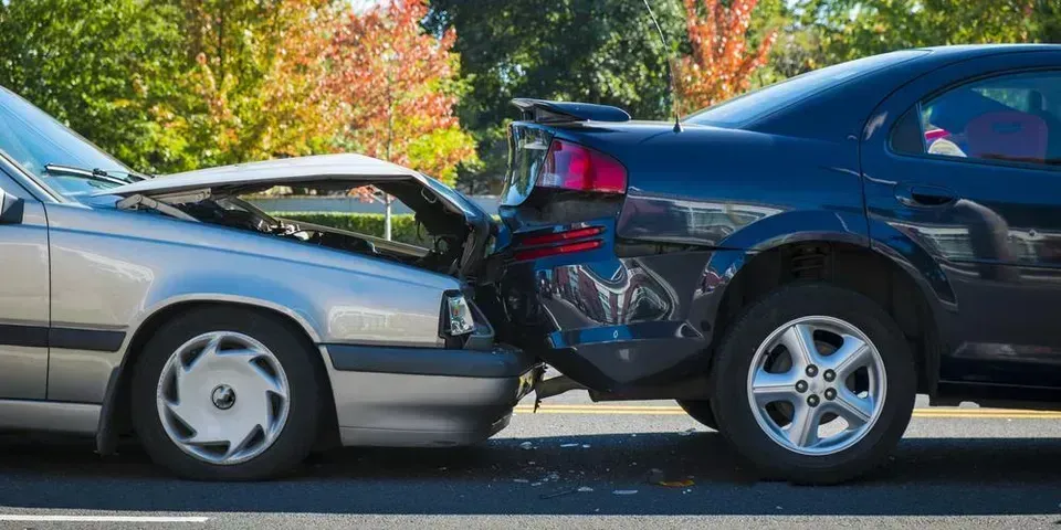 A silver sedan crashed into the rear of a dark-colored car on an outdoor road.