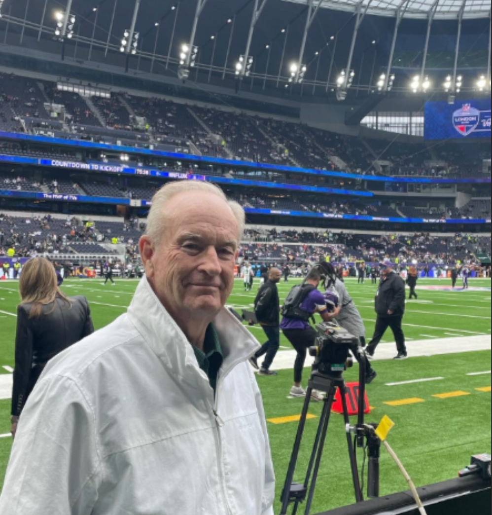 A man in a white jacket is standing on a football field