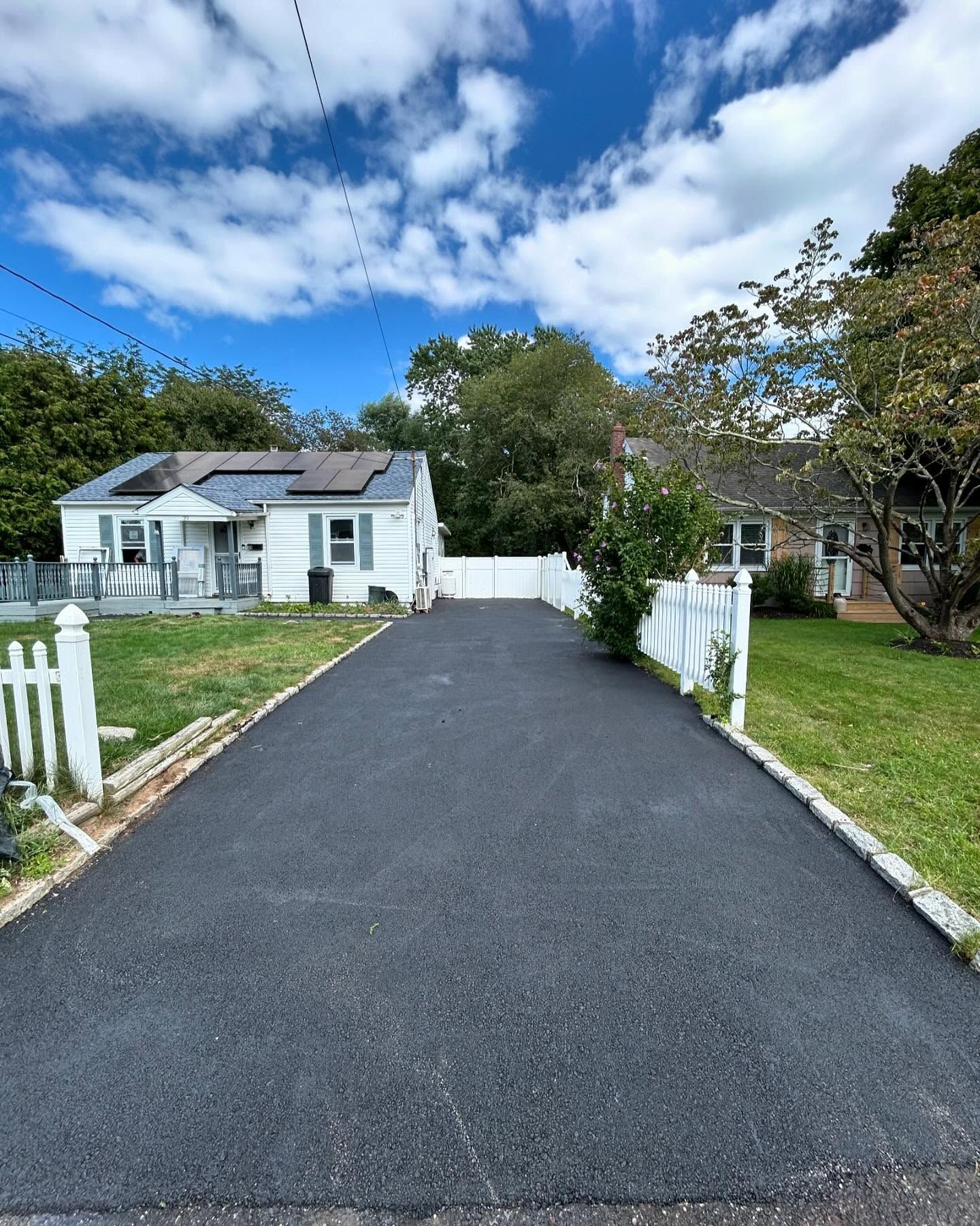 A driveway leading to a house with a white picket fence
