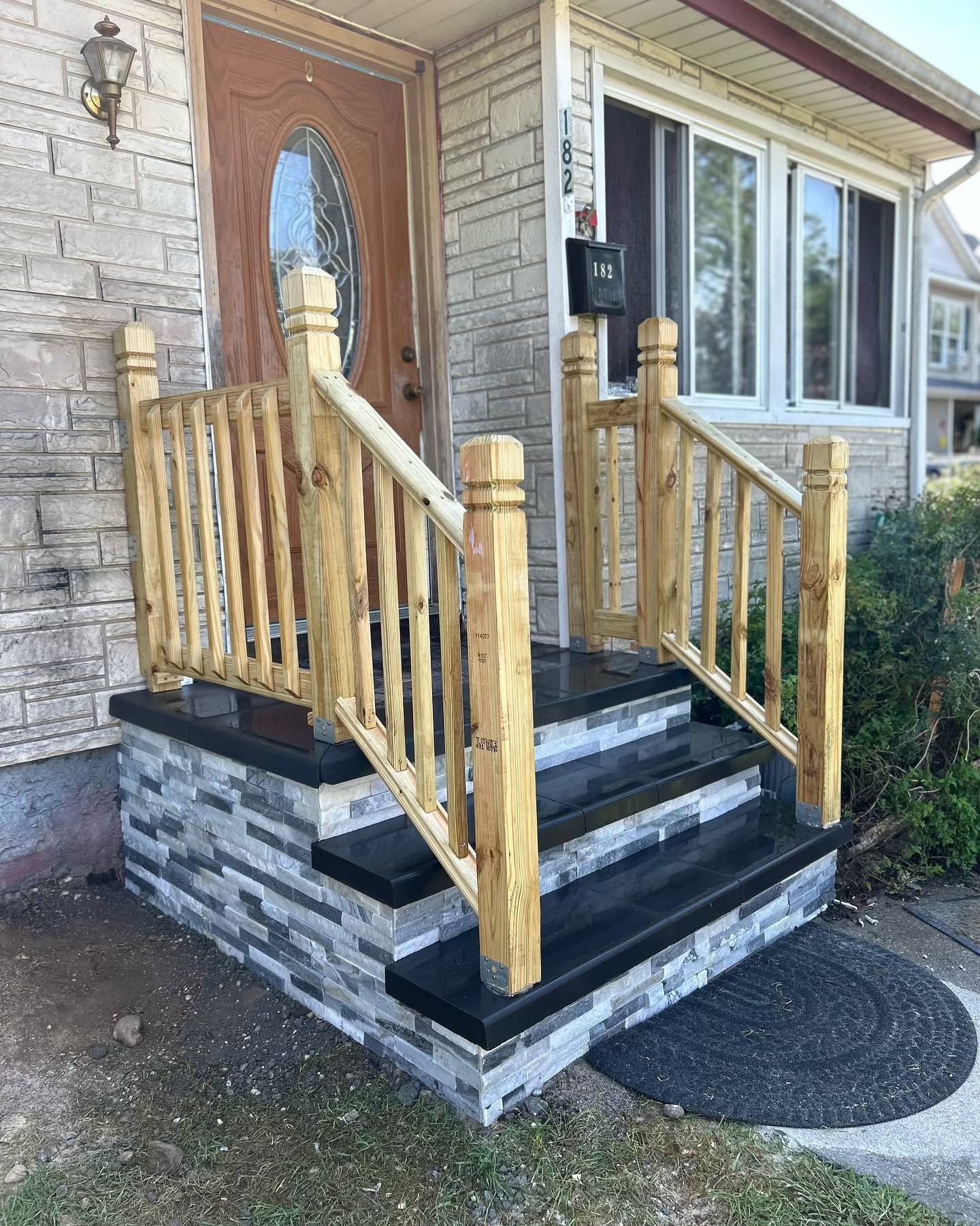 A wooden porch with stairs and a wooden railing in front of a brick house.