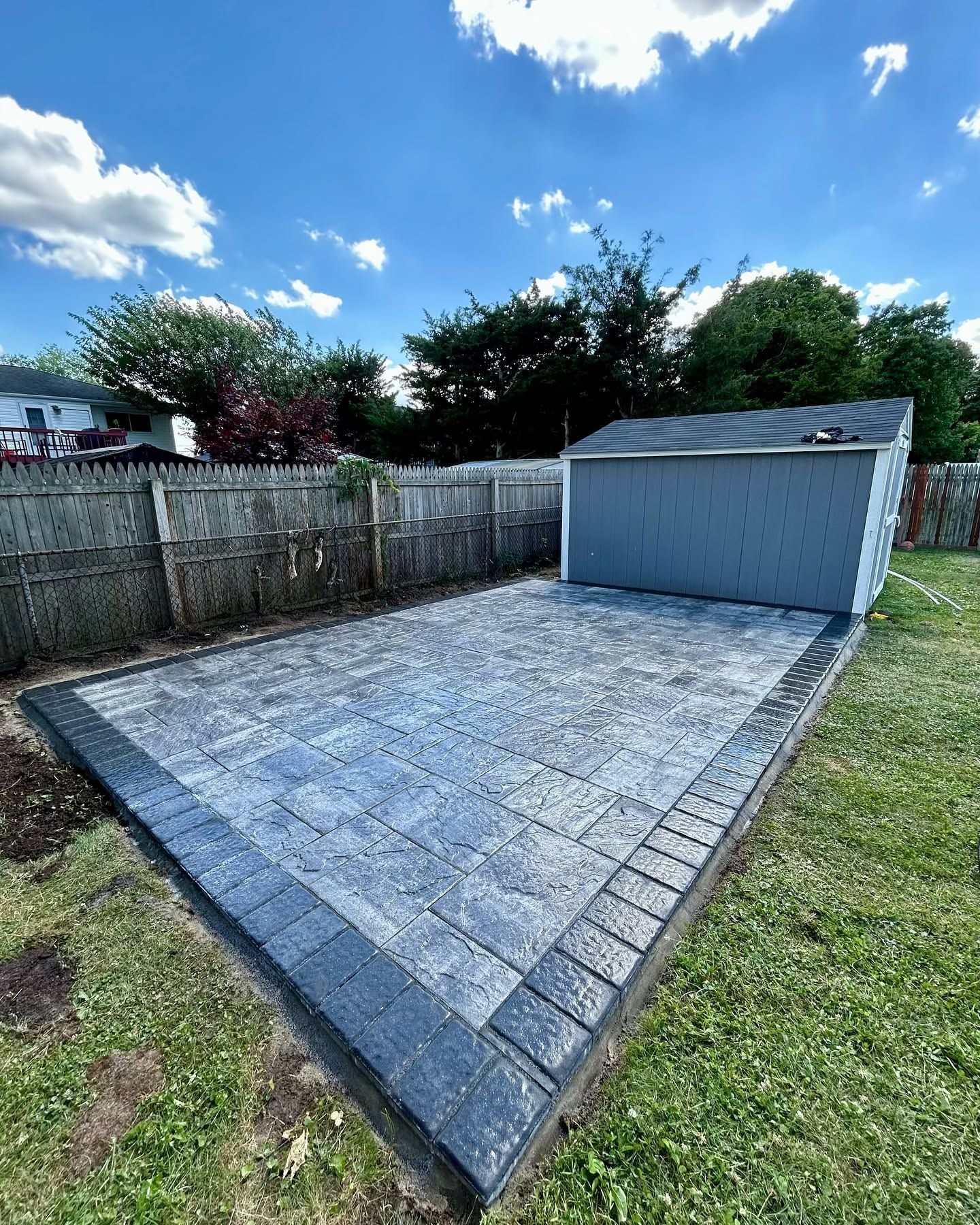 There is a shed in the backyard with a patio in front of it.