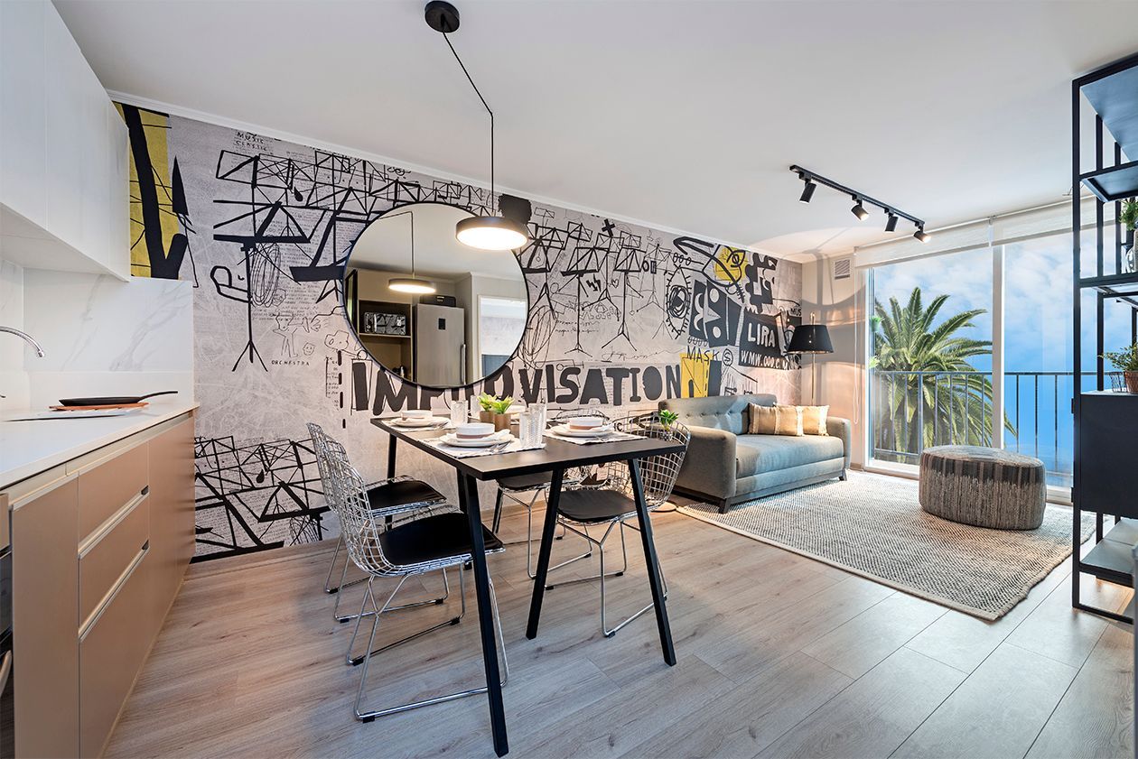Cocina y comedor modernos de planta abierta con obras de arte en la pared, espejo redondo y un rincón de estar soleado.