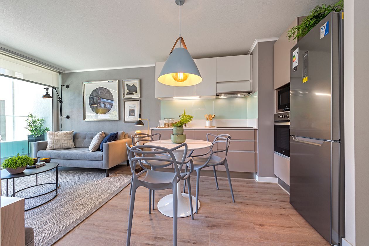Cocina y sala de estar modernas de planta abierta con sofá gris, mesa de comedor, lámpara colgante.