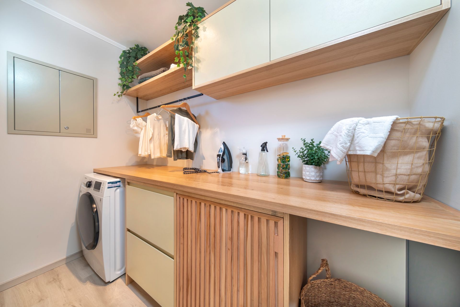 Lavadero minimalista con estanterías de madera, fregadero, lavadora y armarios blancos en una pared clara.