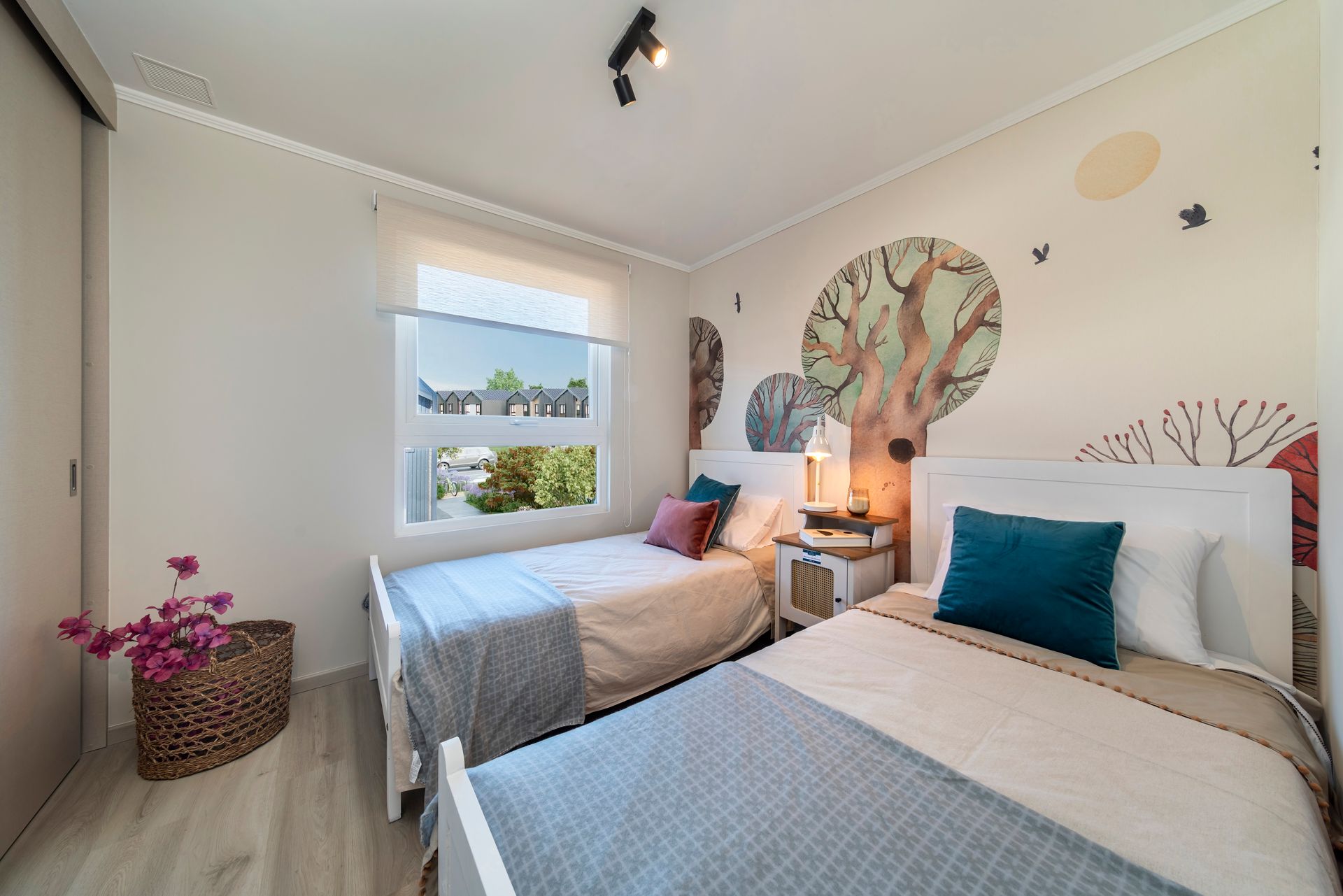 Habitación doble luminosa con dos camas, almohadas color turquesa y vista a la ventana en tonos neutros suaves.