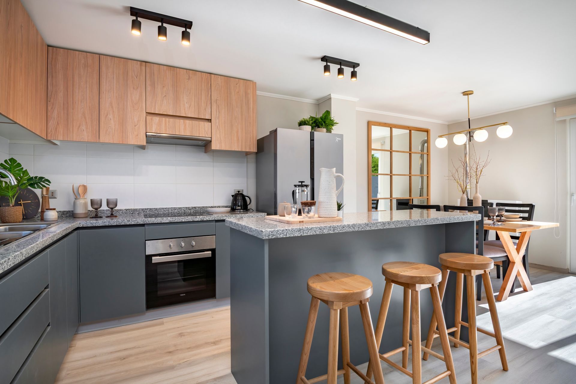 Cocina moderna con isla gris, armarios de madera, taburetes de bar y lámparas colgantes.