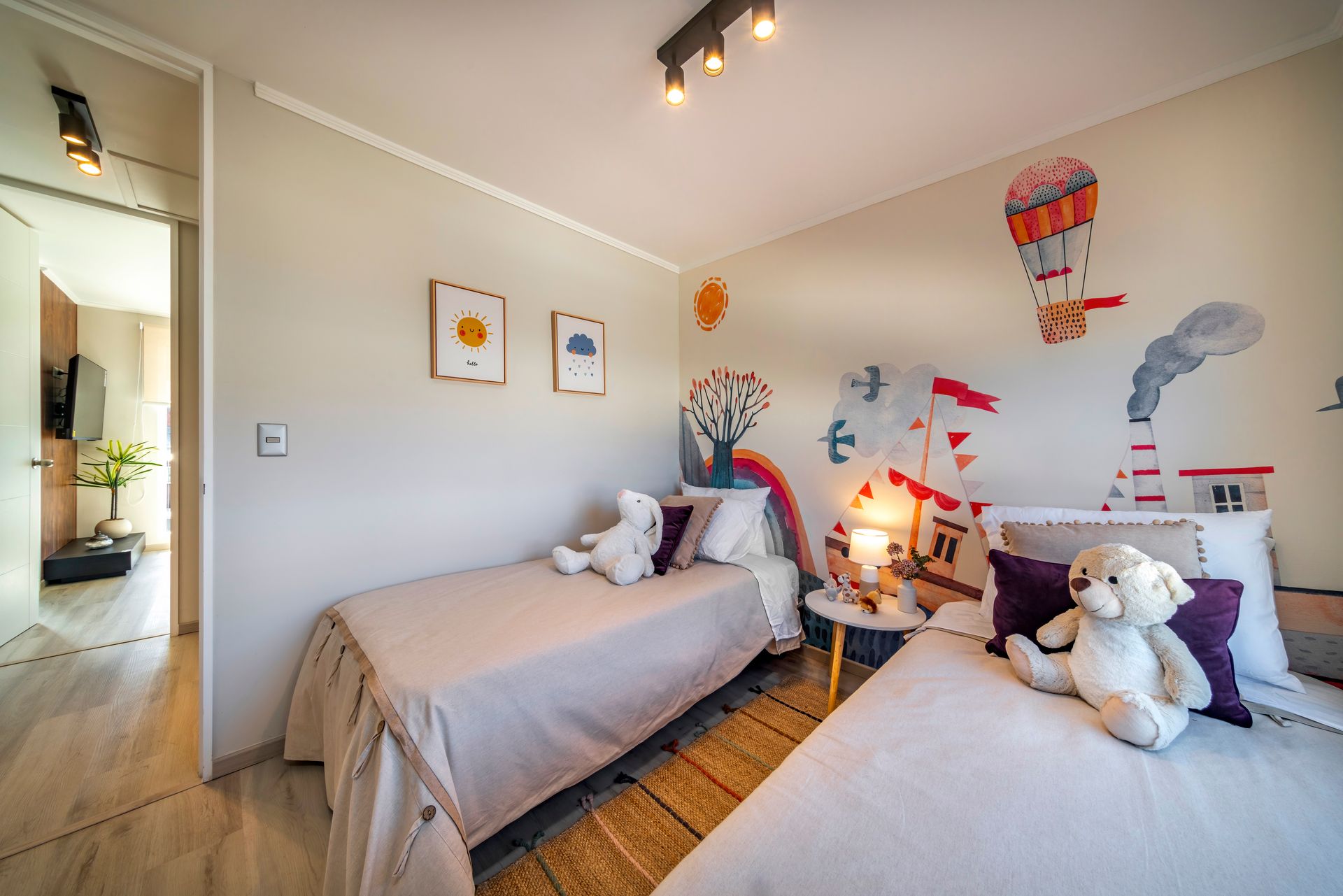 Habitación doble luminosa con dos camas, ositos de peluche, vinilos decorativos en la pared e iluminación cálida y suave.