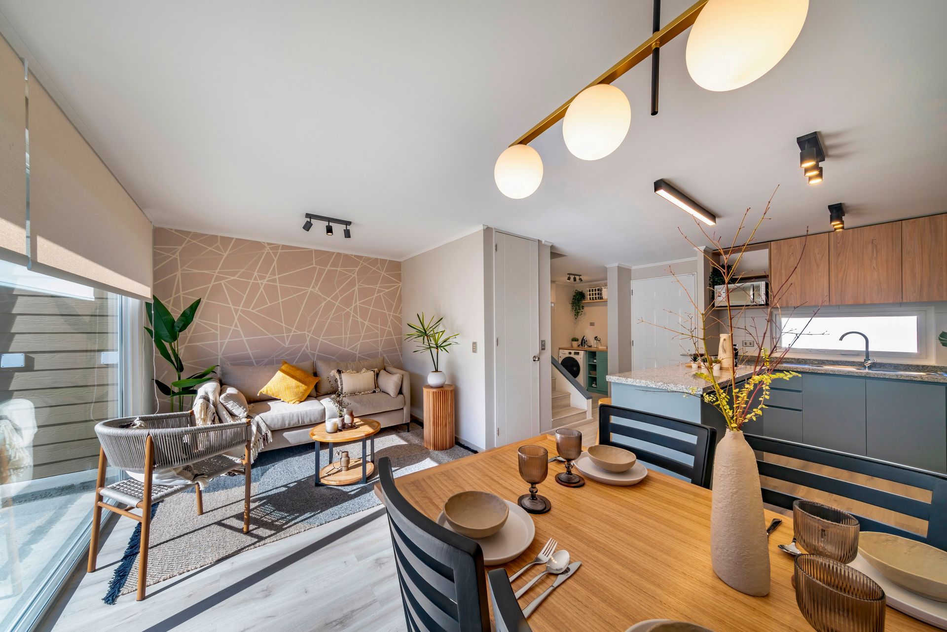 Salón-comedor moderno de planta abierta con muebles de madera, alfombra a rayas y grandes ventanales.