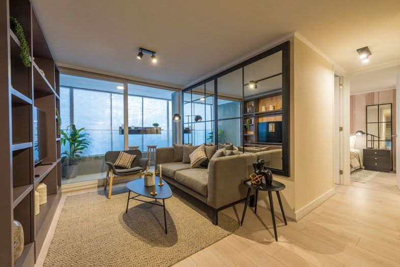 Sala de estar moderna con sofá gris, mesa de centro, mampara de cristal y vistas a la ciudad a través de grandes ventanales.