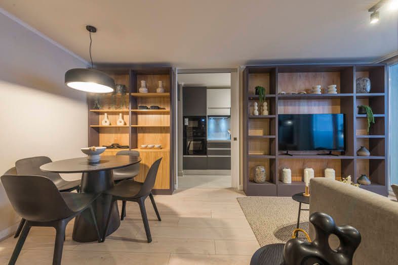Salón-comedor moderno con mesa negra, estanterías empotradas, televisor e iluminación cálida.