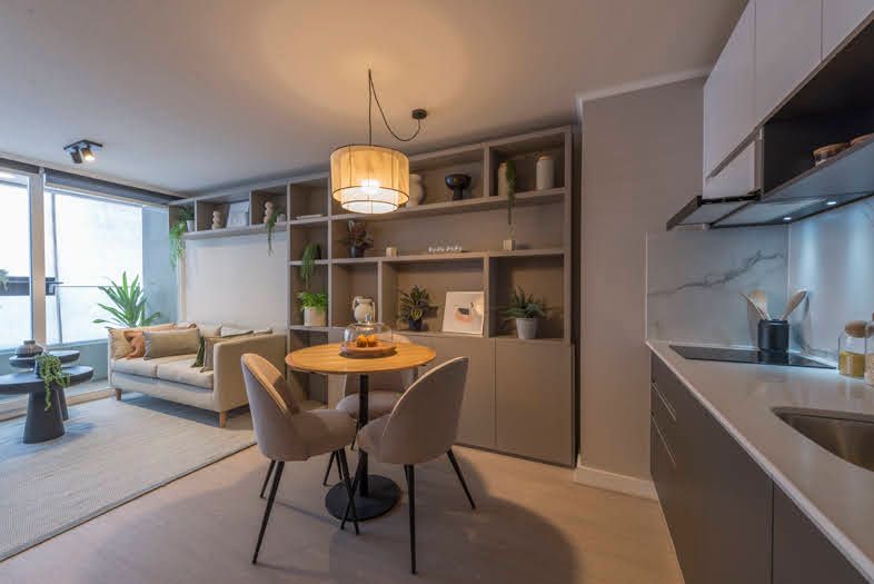 Cocina y comedor modernos de planta abierta con sofá, iluminación cálida y decoración neutra.