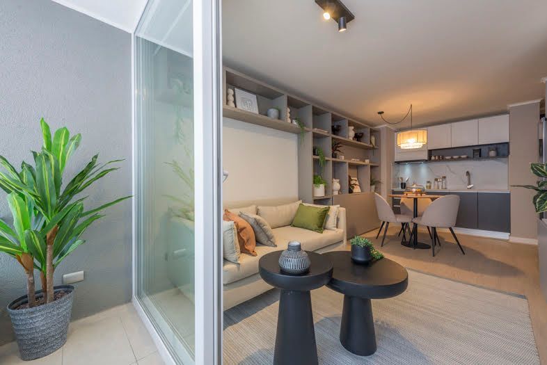 Salón-cocina moderno de planta abierta con vistas al balcón, sofá gris y mesas nido negras.