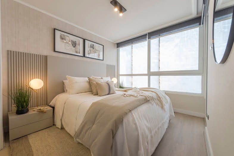 Dormitorio con cama, mesita de noche, gran ventanal y paneles decorativos de pared en tonos neutros.