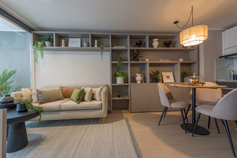 Salón moderno de planta abierta con sofá, estanterías, mesa de comedor e iluminación ambiental cálida.