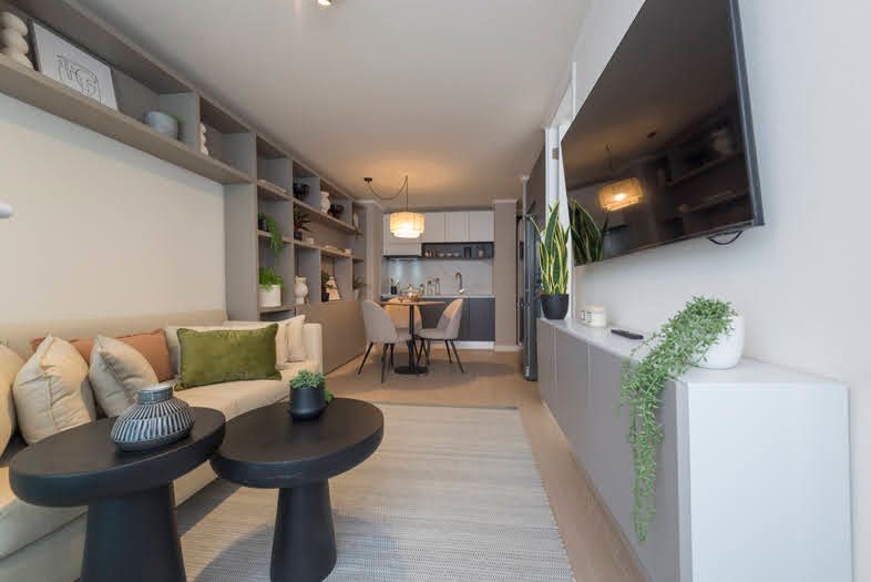Apartamento tipo estudio moderno con sofá, mesas de centro, televisor de pared y rincón para comer.