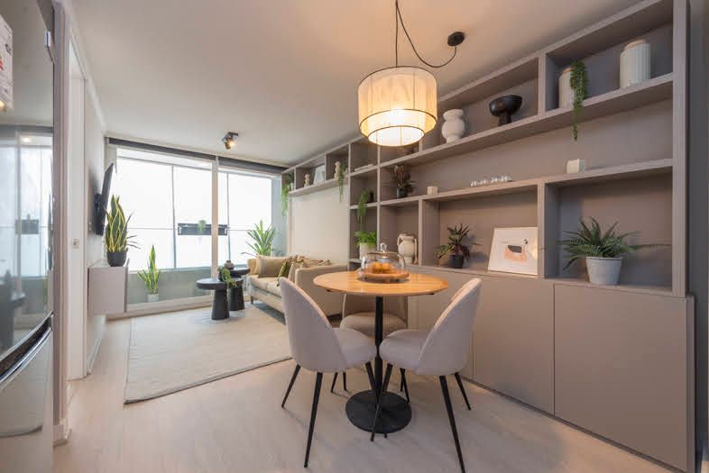 Comedor moderno con mesa redonda, cuatro sillas, estanterías empotradas.