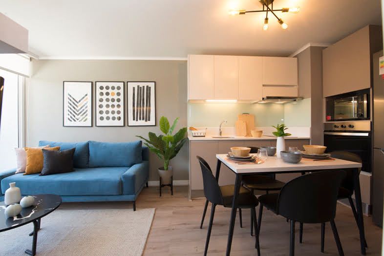 Salón y cocina modernos de planta abierta con sofá azul, mesa de comedor e iluminación cálida.