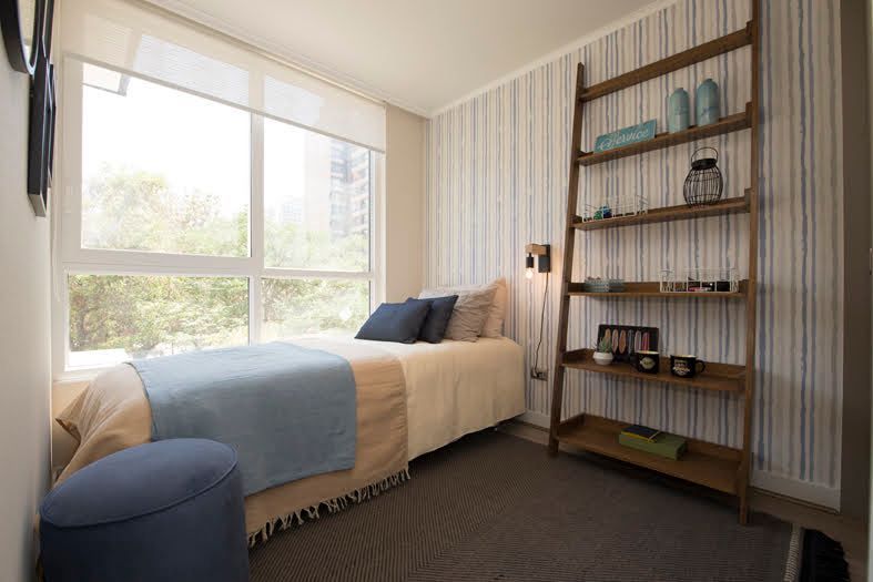 Habitación luminosa con una cama junto a una gran ventana y una estantería alta de madera a la derecha.