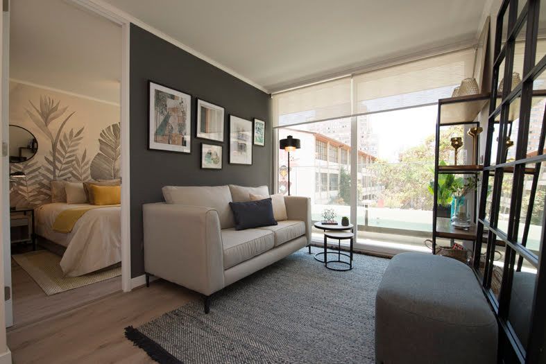 Sala de estar moderna con sofá gris, ventana grande, arte en la pared.