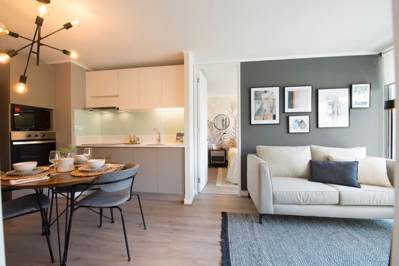 Salón-comedor diáfano con sofá gris, mesa de comedor, cocina y cuadros enmarcados en la pared.
