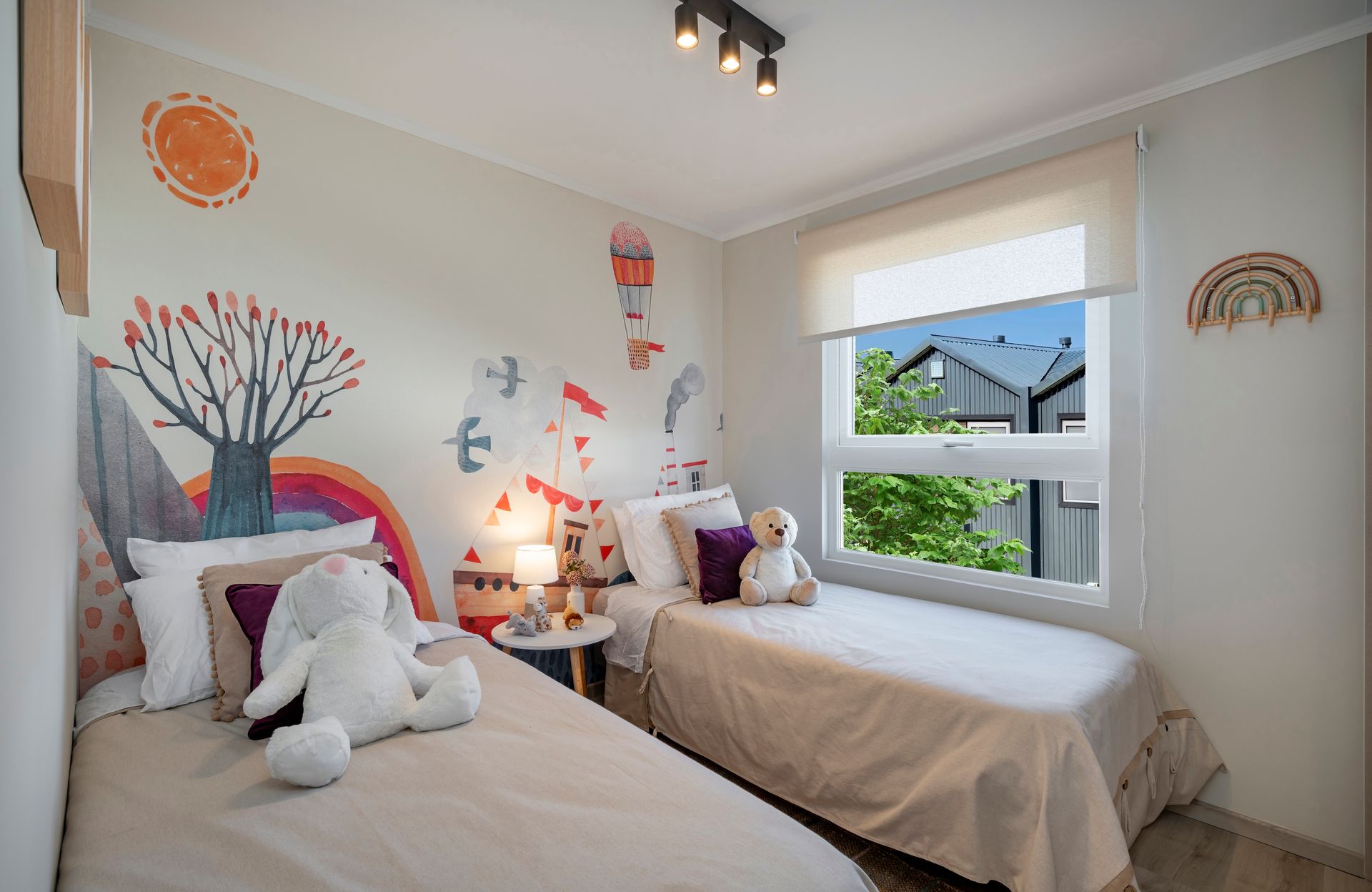 Habitación infantil, coloridos vinilos decorativos en la pared y una ventana con vistas a una casa y vegetación.