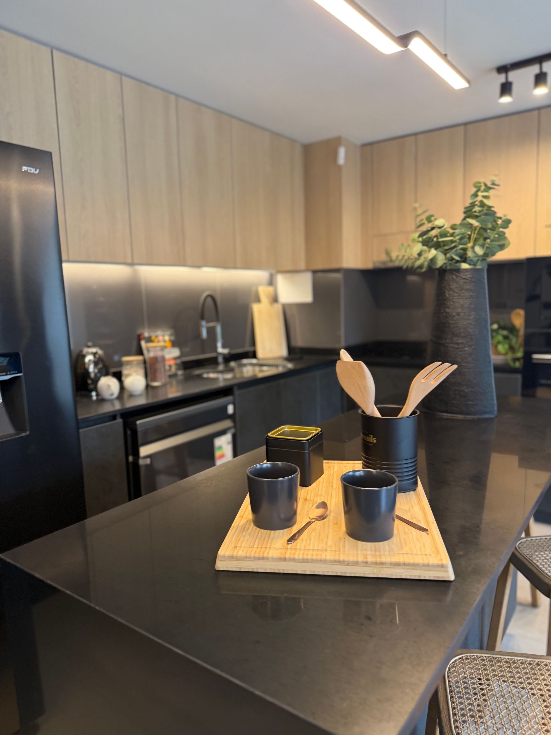 Cocina moderna con isla negra, armarios de madera y una bandeja con tazas y utensilios sobre la encimera.