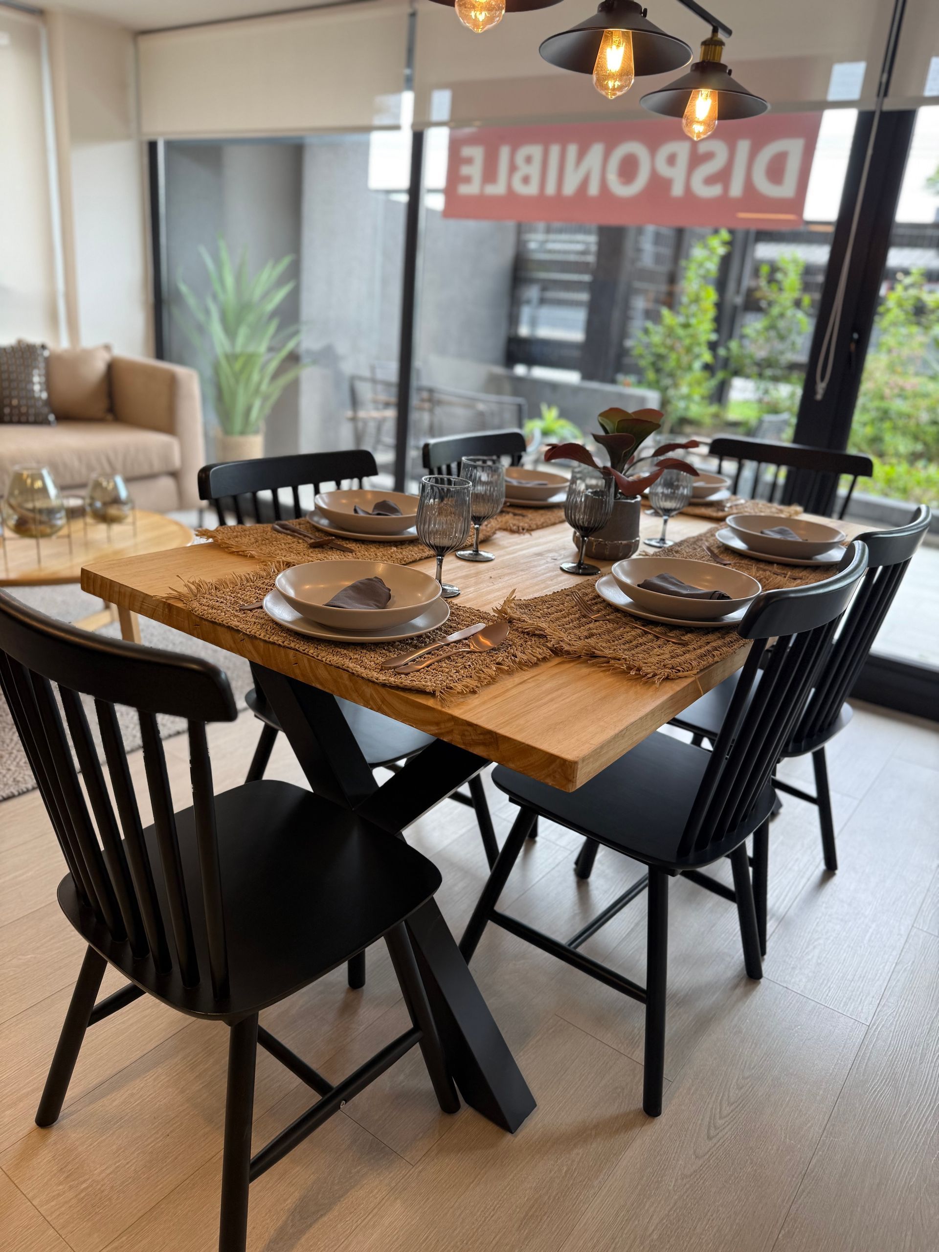 Mesa de comedor para cuatro personas en una habitación luminosa y moderna con sillas negras y manteles individuales tejidos.