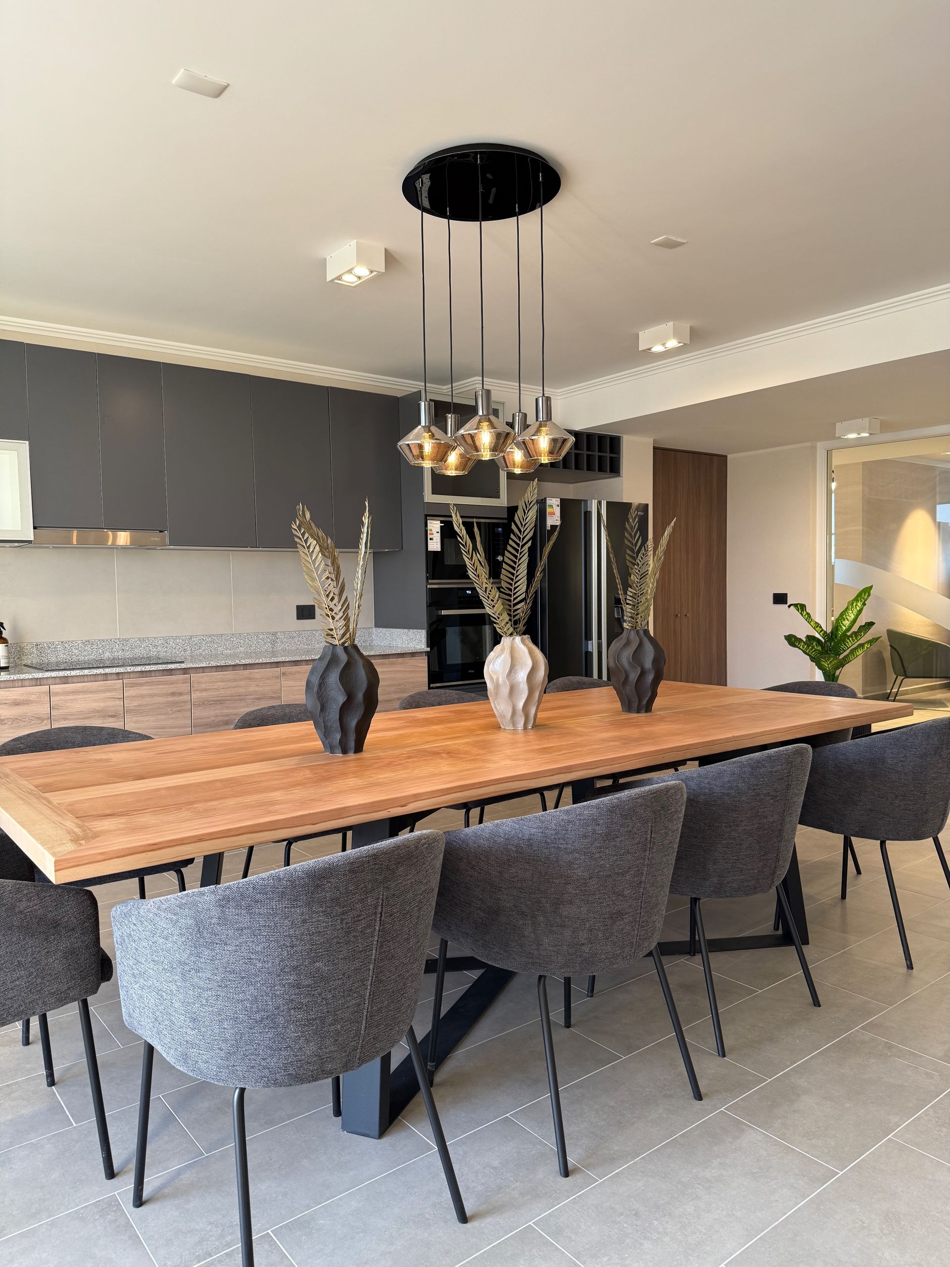 Cocina moderna con isla de madera, armarios grises, lámpara colgante y taburetes tapizados.